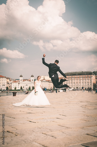 Sposo felice che salta in alto di fronte alla sposa - Trieste (Italia) Molo Audace