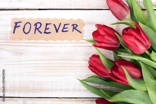 word FOREVER and bouquet of tulips on wooden background