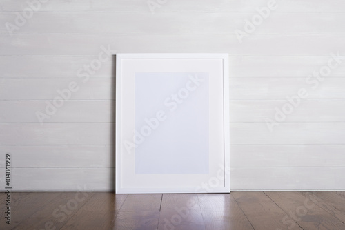 White picture frame sitting on wooden floor leaning on a white wall