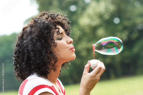 Tableau sur toile Portrait of beautiful woman blowing bubbles in park.