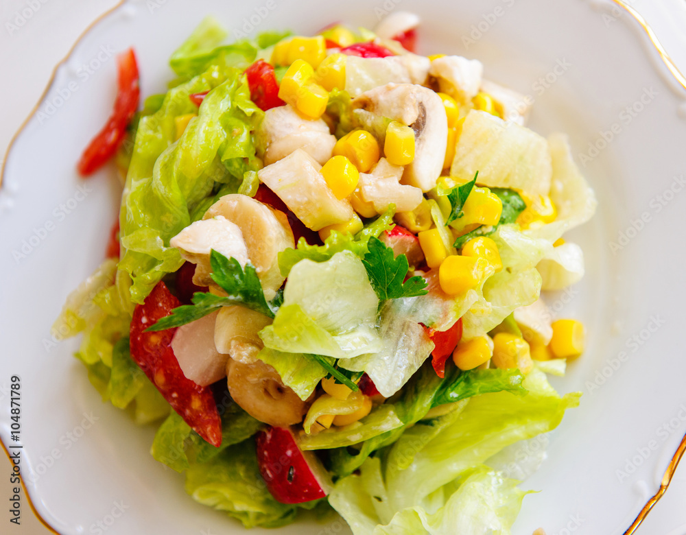 Homemade fresh salad with champignon, tomatoes, corn, lettuce, and feta cheese on white dish - seen from above