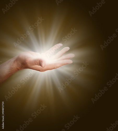 Connecting to the Divine Source - a male hand with palm open glowing with light energy on a dark warm brown background with plenty of copy space