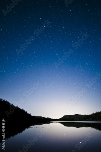 the sky at night over a calm lake in mountains