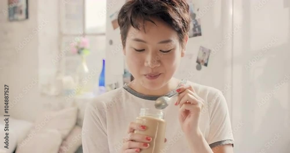 Asian girl indulging eating peanut butter from jar using spoon Asian girl indulging eating peanut butter from jar using spoon