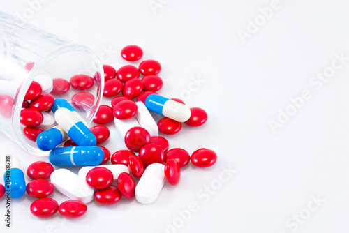 Red, blue and white pills in small cup on a white background