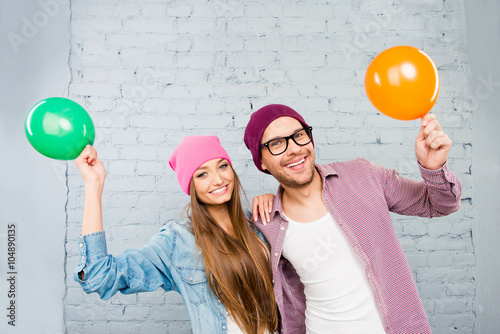 Positive couple in love in caps and glasses holding balloons photo