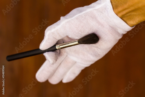 White gloved hand holding a paintbrush.