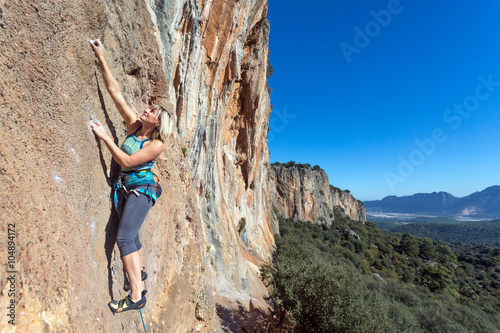 Female extreme Climber hanging on high vertical Rock