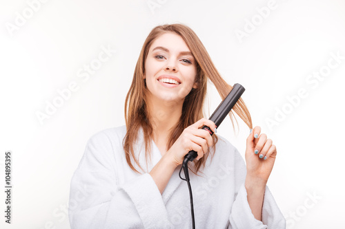 Cheerful attractive young woman straightening her hair with  straightener photo