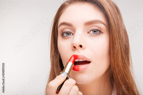 Charming tender  woman in bathrobe doing makeup with red lipstick