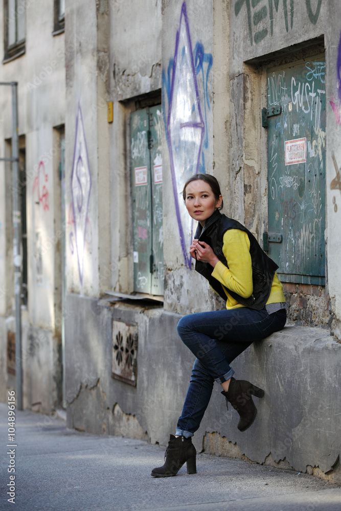 Beautiful Asian woman in yellow sweater and jeans sitting at a house with graffiti
