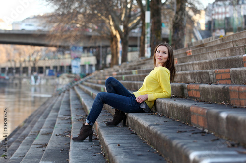 Beautiful Asian woman in yellow sweater sitting at a river in a European city