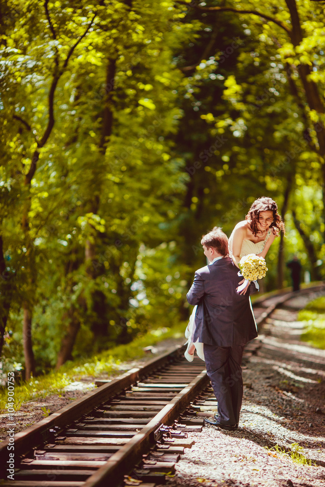 Fototapeta premium Happy newlywed romantic couple walking on rails in the park