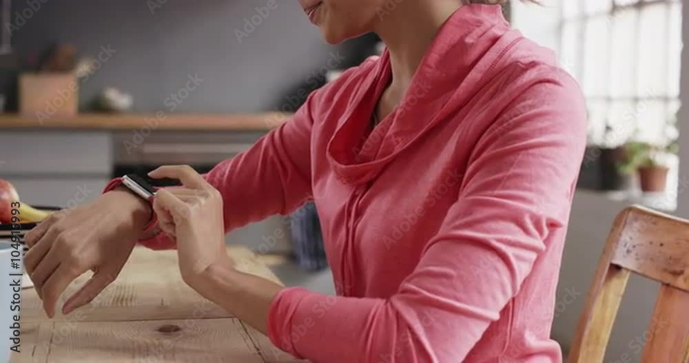 Mixed race sporty woman using smart watch at home drinking coffee