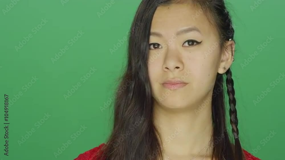 Young Asian woman looking around and making silly faces, on a green screen studio background Young Asian woman looking around and making silly faces, on a green screen studio background