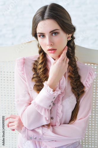 Portrait of an elegant beautiful young woman with trendy braids hairstyle dressed in faded pink stylish blouse