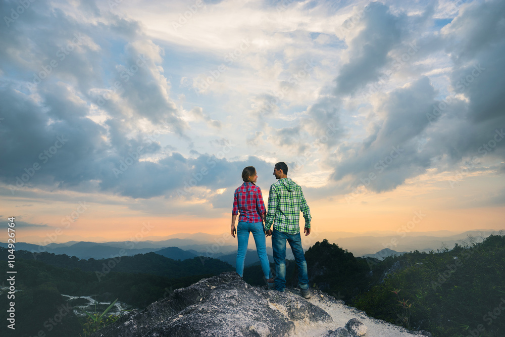 Fototapeta premium Couple on the top of mountain with beautiful sunset background. Back view.
