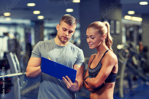 smiling young woman with personal trainer in gym photo