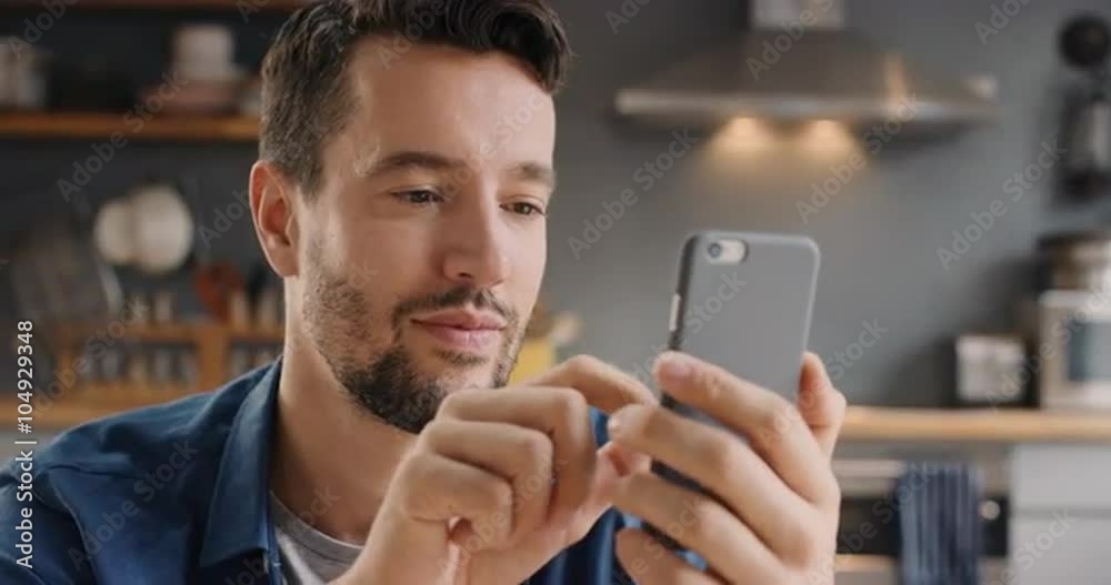 Attractive man at home using smart phone in kitchen sending message on social media