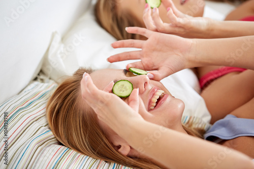 happy young women with cucumber mask lying in bed