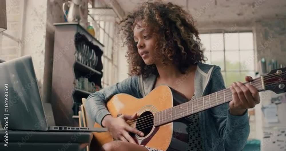 Attractive mixed race young girl learning to play guitar using laptop computer 