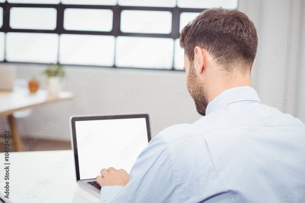 Businessman working on laptop at desk in office Businessman working on laptop at desk in office