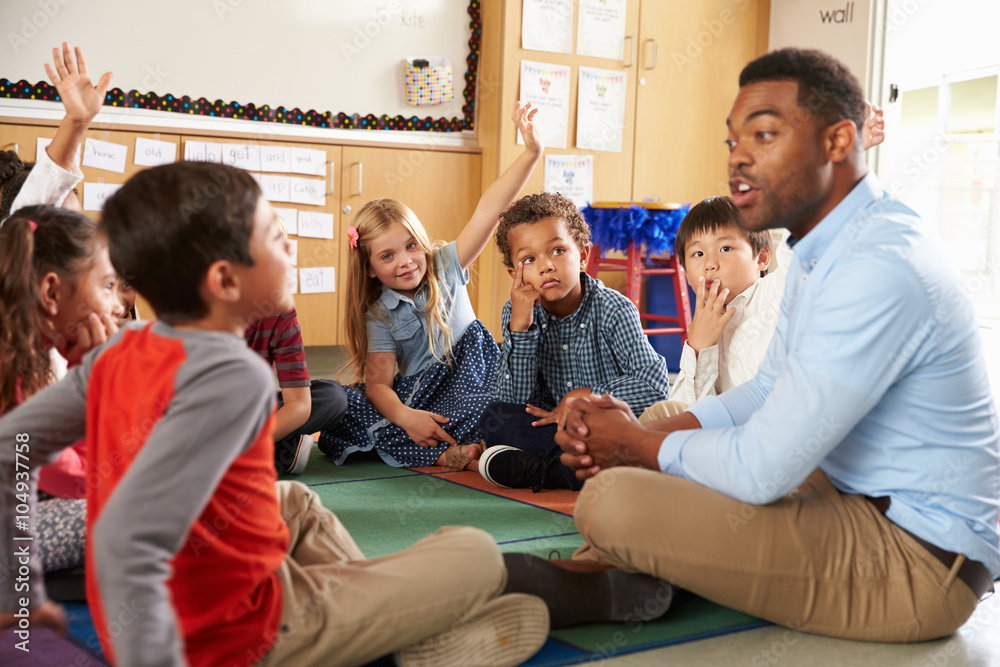 Fototapeta premium Elementary school kids and teacher sit cross legged on floor