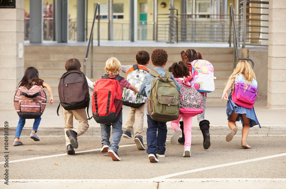 Obraz premium Elementary school kids running into school, back view