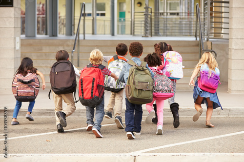 Elementary school kids running into school, back view