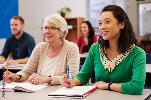 Two women sharing a desk at an adult education class look up