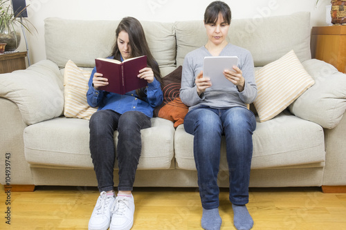 Mother and daughter reading a book and a tablet

