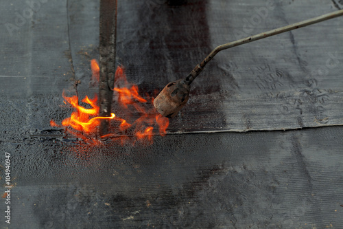 waterproofing roll bituminous material in the trench. construction worker manufacturer uses a gas burner propane tank fire.