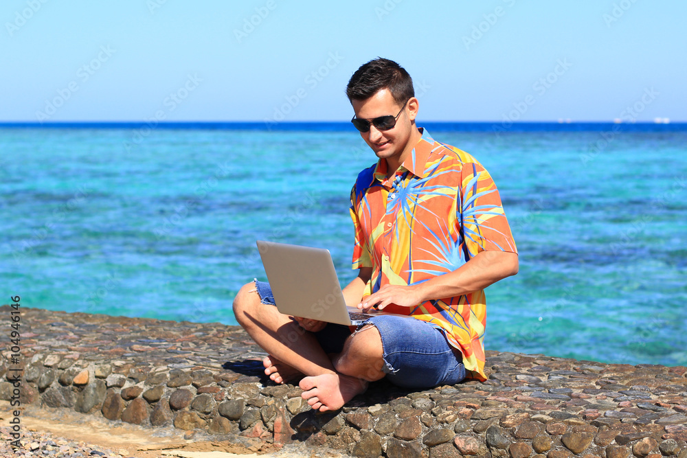 young man, freelancer, working at his laptop computer at the sea 