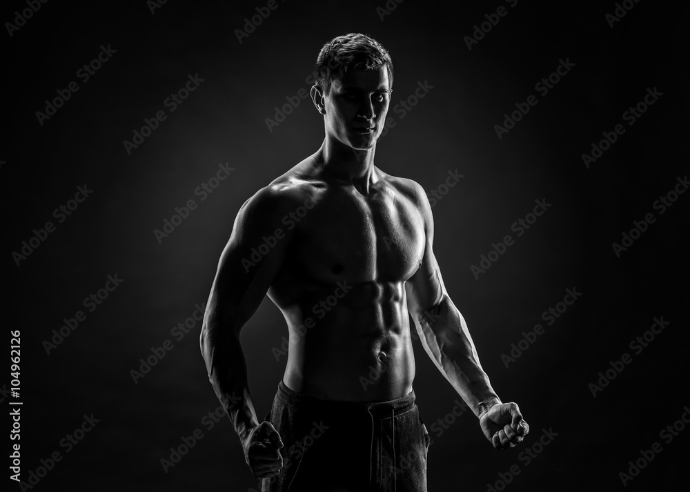 Naklejka premium Sexy shirtless bodybuilder posing, looking at camera on black ba