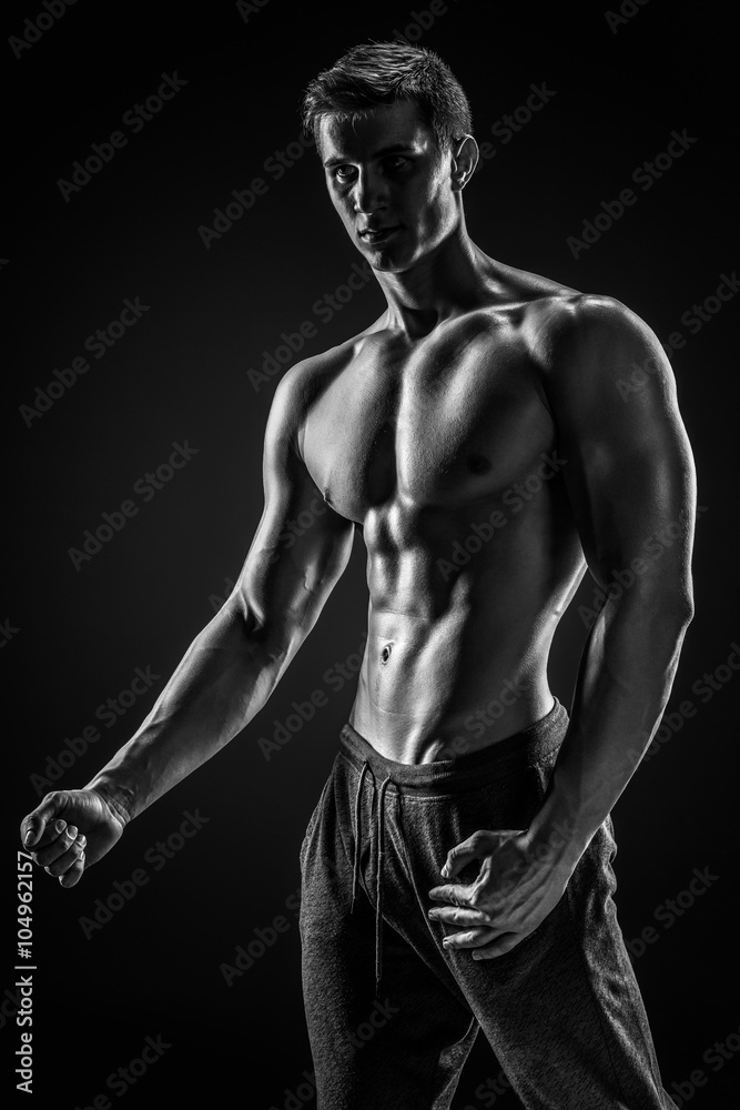 Sexy shirtless bodybuilder posing, looking at camera on black ba Sexy shirtless bodybuilder posing, looking at camera on black ba