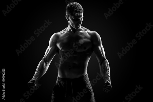 Sexy muscular man posing with naked torso on black background