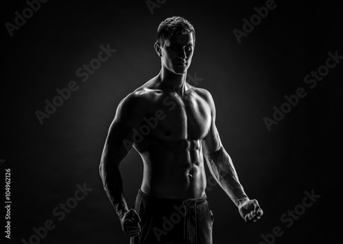 Sexy shirtless bodybuilder posing, looking at camera on black ba