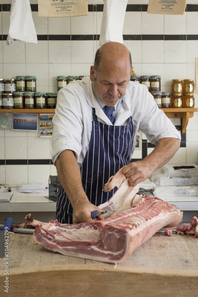Butcher pulling fat off a large cut of pork