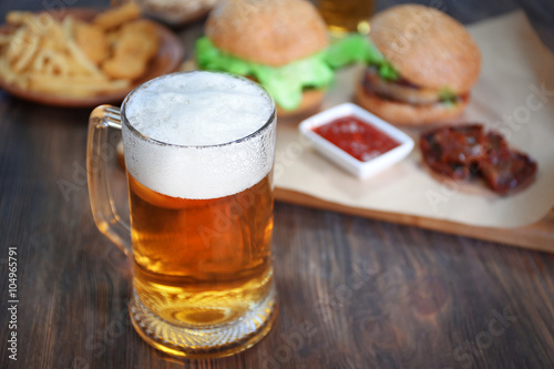 Glass mug of light beer with snacks on dark wooden table, close up