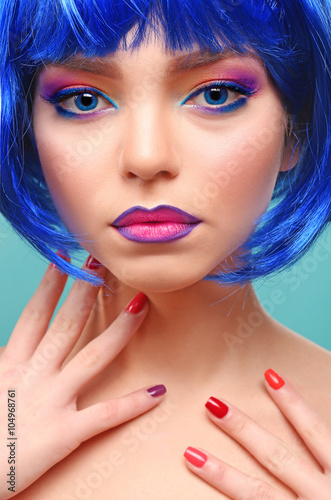 Beautiful girl with colorful makeup  manicure and wig on blue background