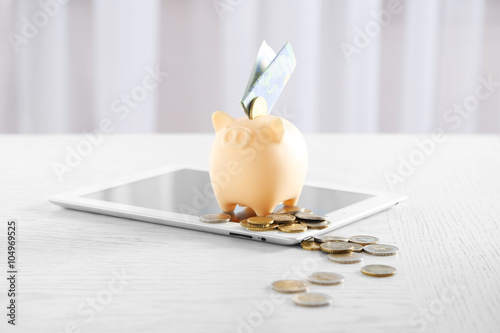 Piggy bank with tablet and money on table indoors