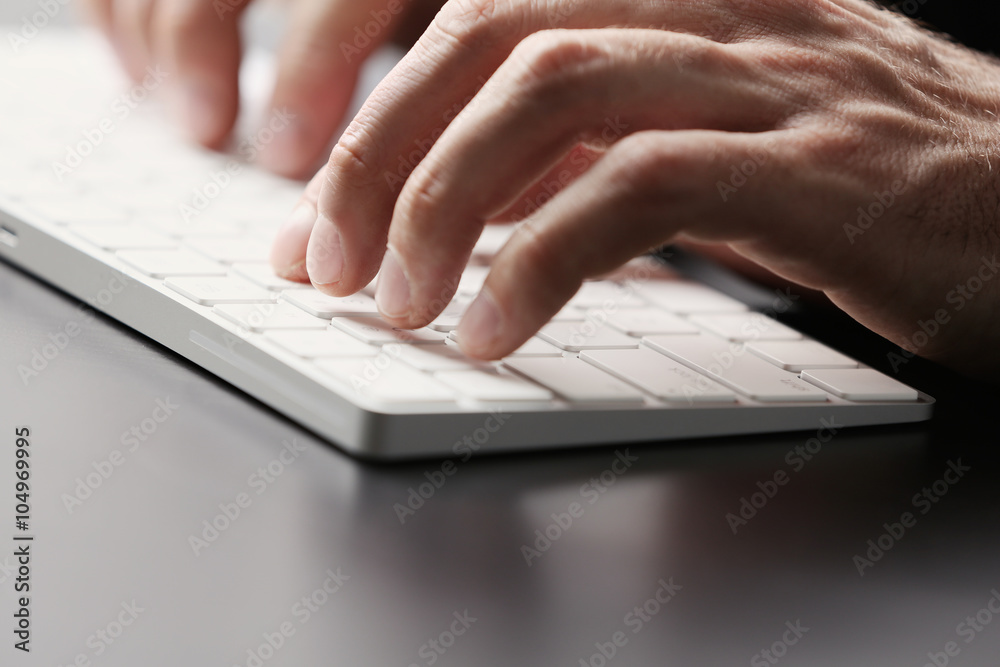 Male hands typing on wireless keyboard at table closeup