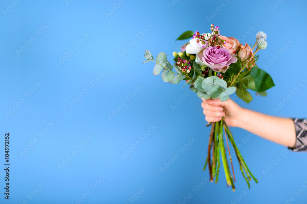 Fototapeta premium Female hand holding a bouquet of roses on blue background