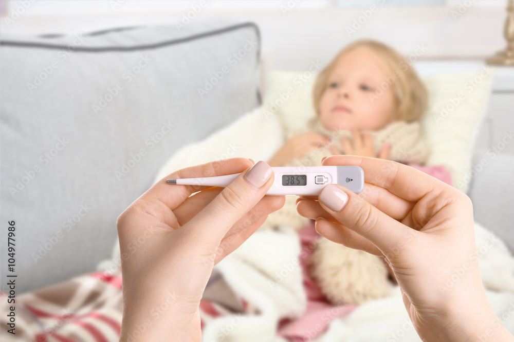 Little girl with sore throat lying in bed and hands with thermometer Little girl with sore throat lying in bed and hands with thermometer