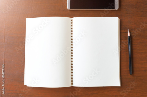 Blank note book with pencil and smartphone on wooden table backg