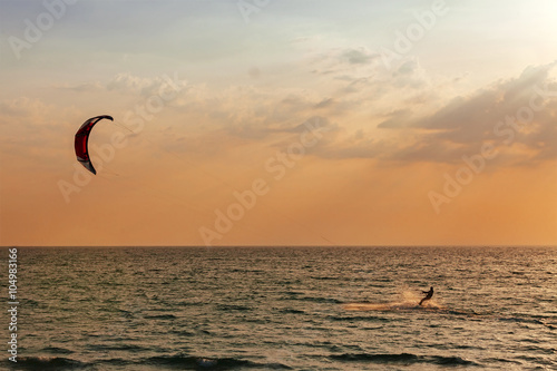 Kite surfer sailing in the sea at sunset