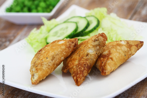 Indian samosas with green side salad on white plate, closeup
