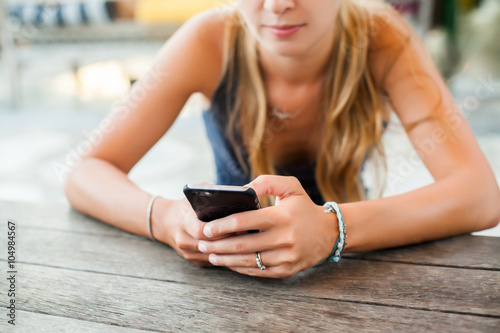 young cute girl hipster, sitting at a cafe holding a smart phone, answering texts, phone calls, letters, posts photos in instagram, outdoor portrait, close up, elaborated and bracelets on the hands