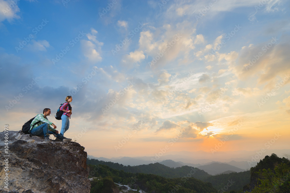 Young backpackers enjoying a valley view from top of a mountain in sunset. Travel concept.