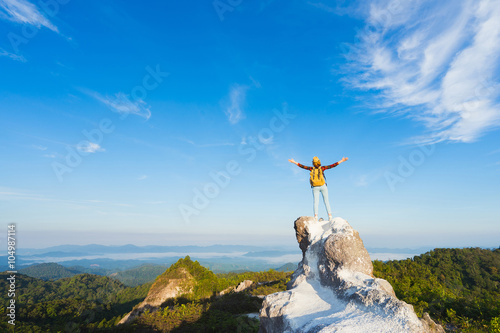 Hiker with backpack standing on top of the mountain and enjoying valley view